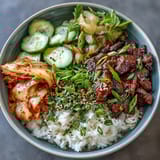 Vibrant Korean Beef Bowl with seasoned ground beef in spicy gochujang sauce over fluffy rice, topped with crisp pickled vegetables and fresh cucumber slices.  