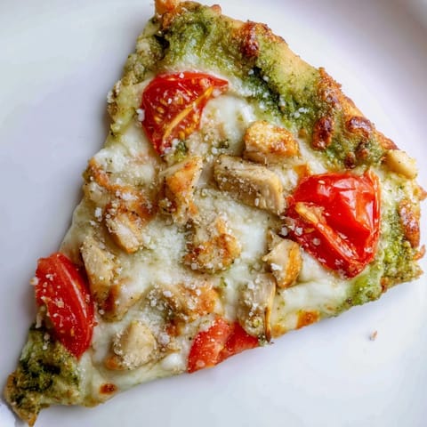 Close-up of a thin-crust chicken pesto pizza with vibrant basil pesto, Parmesan, and bubbling cheese, ready to be served.