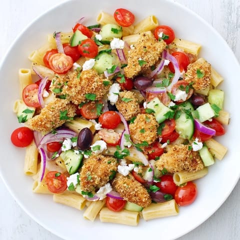 Golden crispy chicken bites rest on a colorful bed of penne pasta tossed with fresh tomatoes, cucumbers, and tangy feta cheese.  