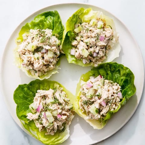 Golden chicken salad mixture spooned into green lettuce leaves, topped with fresh dill and a creamy, tangy dill pickle dressing.  