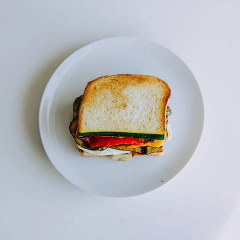 Slice of Roasted Veggie Caprese Grilled Cheese with juicy tomatoes, fresh basil, and colorful roasted zucchini layered inside.