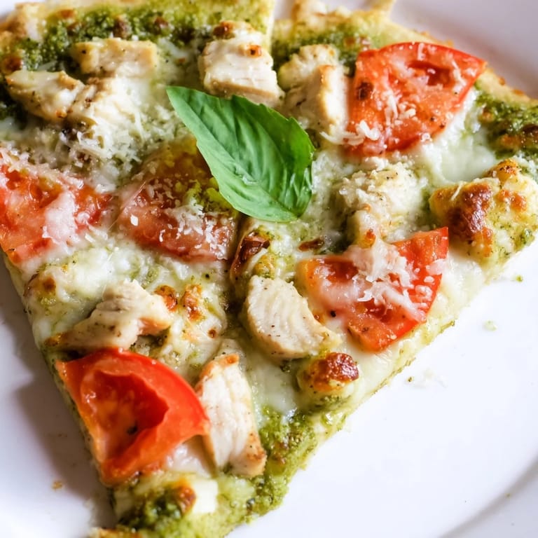 A rustic baked chicken pesto pizza with fragrant basil, diced chicken, and tomatoes on a baking sheet, perfect for dinner.