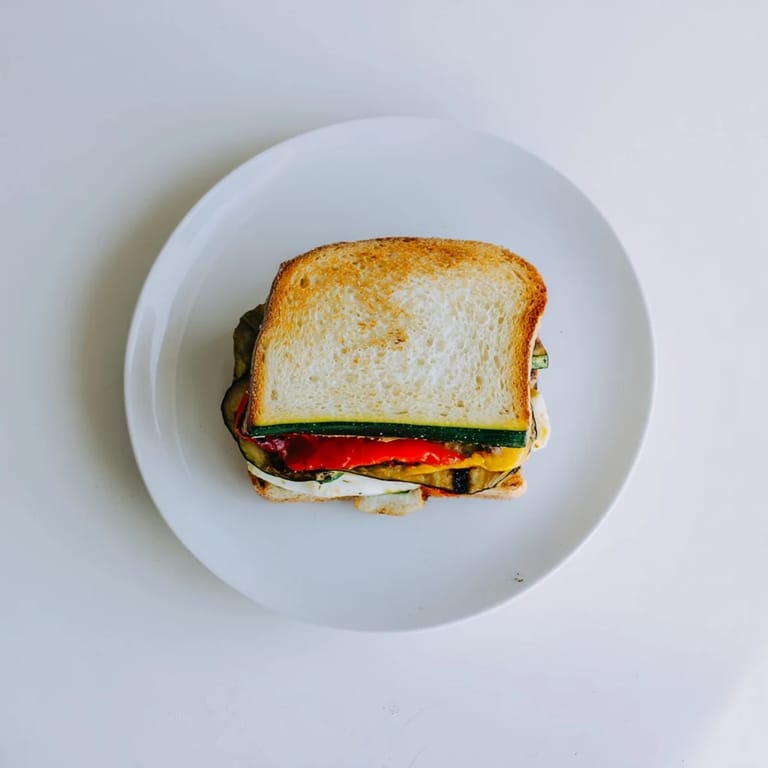 Slice of Roasted Veggie Caprese Grilled Cheese with juicy tomatoes, fresh basil, and colorful roasted zucchini layered inside.