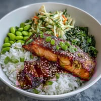Vibrant Asian-inspired salmon bowl with soy-ginger glazed fillets, steamed rice, and colorful julienned vegetables, garnished with sesame seeds.  